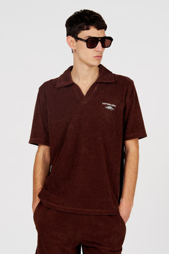 Polo marron de Le Fabuleux Marcel de Bruxelles, avec un motif texturé subtil, vue de dos, combinée avec un pantalon assorti et des lunettes de soleil noires.