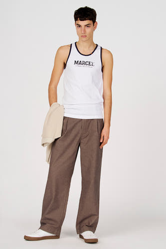 Pantalon marron de couleur de Le Fabuleux Marcel de Bruxelles, avec jambes larges et porté avec une chemise blanche et des baskets blanches.