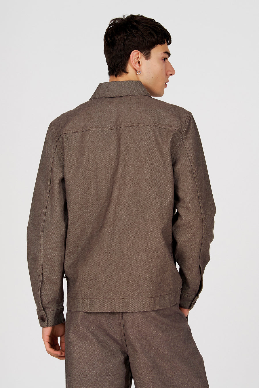 Manteau court marron de Le Fabuleux Marcel de Bruxelles, vu de dos, avec une subtile texture à chevrons et un pantalon assorti.