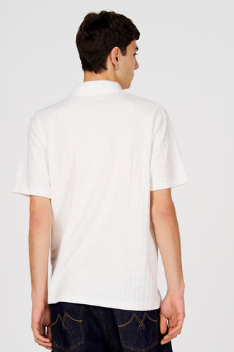 Wit poloshirt van Le Fabuleux Marcel de Bruxelles, met subtiel ruitpatroon, gezien van achteren, gecombineerd met donkere jeans.
