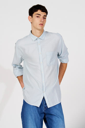 Chemise rayée bleue (manches longues) de Le Fabuleux Marcel de Bruxelles, avec manches retroussées, portée avec un jean bleu foncé.