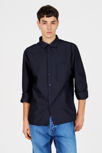 Chemise bleue à manches longues de Le Fabuleux Marcel de Bruxelles, dos, avec manches retroussées et pantalon en jean.