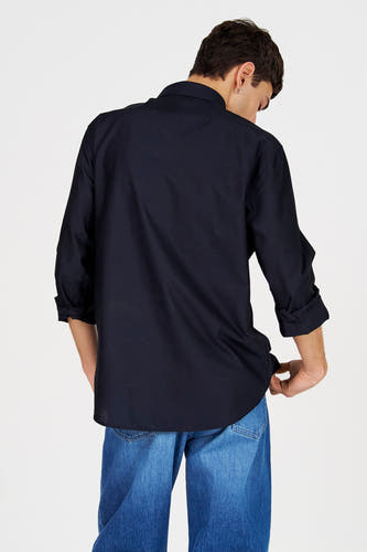 Blauw overhemd met lange mouwen van Le Fabuleux Marcel de Bruxelles, achterkant, met opgerolde mouwen en denim broek.
