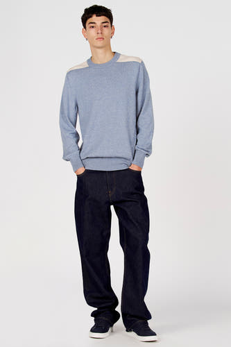 Pull bleu à col rond de Le Fabuleux Marcel de Bruxelles, avec des détails beiges sur les épaules, combiné avec un jean foncé et des baskets.