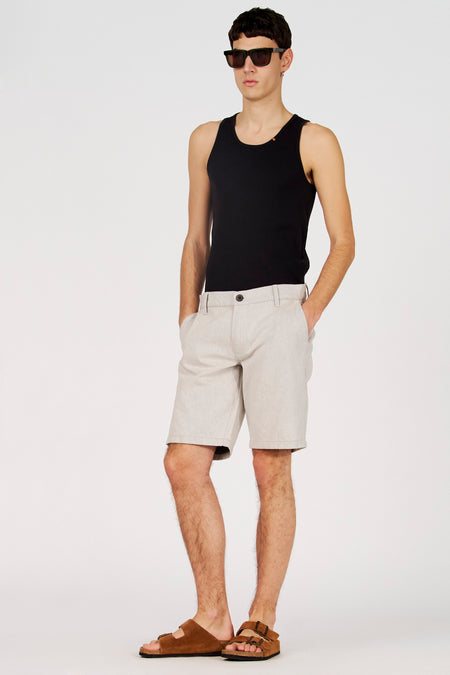 Short écru de Le Fabuleux Marcel de Bruxelles, avec poches insérées et sandales marron.