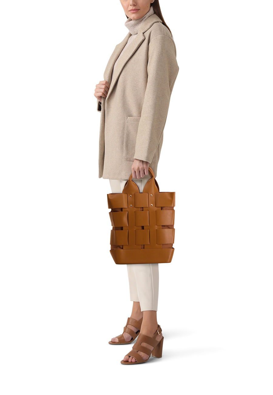 Sac à main brun de Le Fabuleux Marcel de Bruxelles, porté par un modèle avec un manteau beige et des bottes.