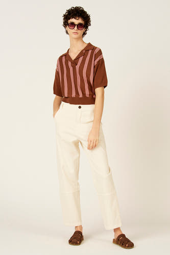Polo marron à manches courtes de Le Fabuleux Marcel de Bruxelles, avec des rayures verticales roses. Porté avec un pantalon de couleur crème et des sandales marron.