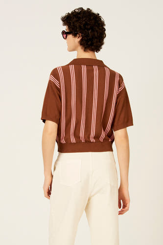 Bruine polo met korte mouwen van Le Fabuleux Marcel de Bruxelles, met roze verticale strepen en gedragen met een witte broek.
