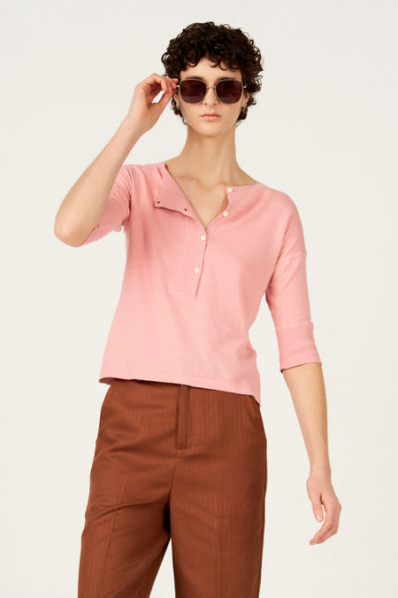 Roze trui met ronde hals van Le Fabuleux Marcel de Bruxelles, met knoopsluiting en bruine broek.
