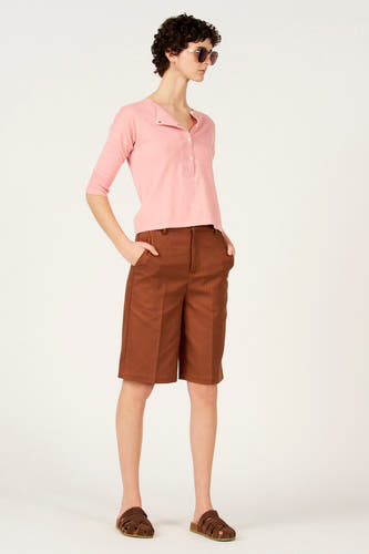 Pull rose à col rond de Le Fabuleux Marcel de Bruxelles, à manches courtes, combiné avec un short marron et des sandales.