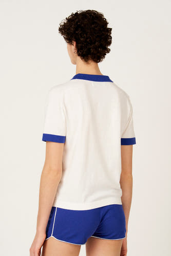 Ecru polo met korte mouwen van Le Fabuleux Marcel de Bruxelles, met blauwe accenten aan kraag en mouwen, en bijpassende blauwe shorts.
