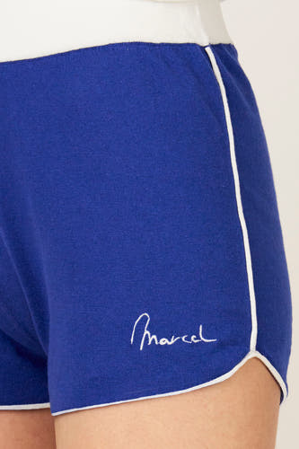 Short bleu de Le Fabuleux Marcel de Bruxelles, avec passepoil blanc et le logo de la marque en lettres blanches.