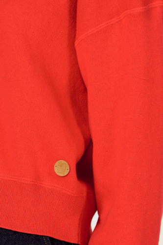 Pull rouge à col rond de Le Fabuleux Marcel de Bruxelles, avec un petit logo rond de la marque sur le côté.