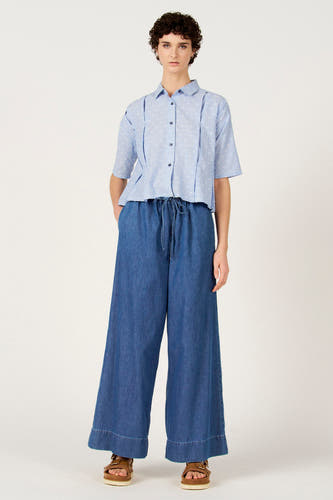 Chemise bleue à rayures à manches courtes de Le Fabuleux Marcel de Bruxelles, avec des pois blancs et portée avec un pantalon ample bleu foncé.