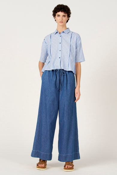 Chemise bleue à rayures à manches courtes de Le Fabuleux Marcel de Bruxelles, avec des pois blancs et portée avec un pantalon ample bleu foncé.