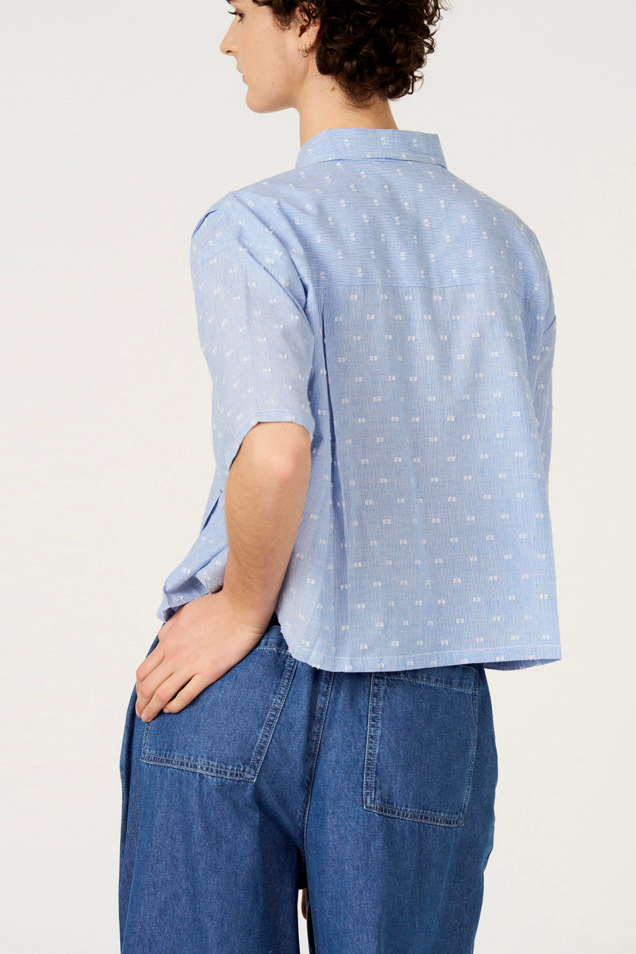 Chemise bleue à rayures à manches courtes de Le Fabuleux Marcel de Bruxelles, avec des pois blancs et un jean décontracté.