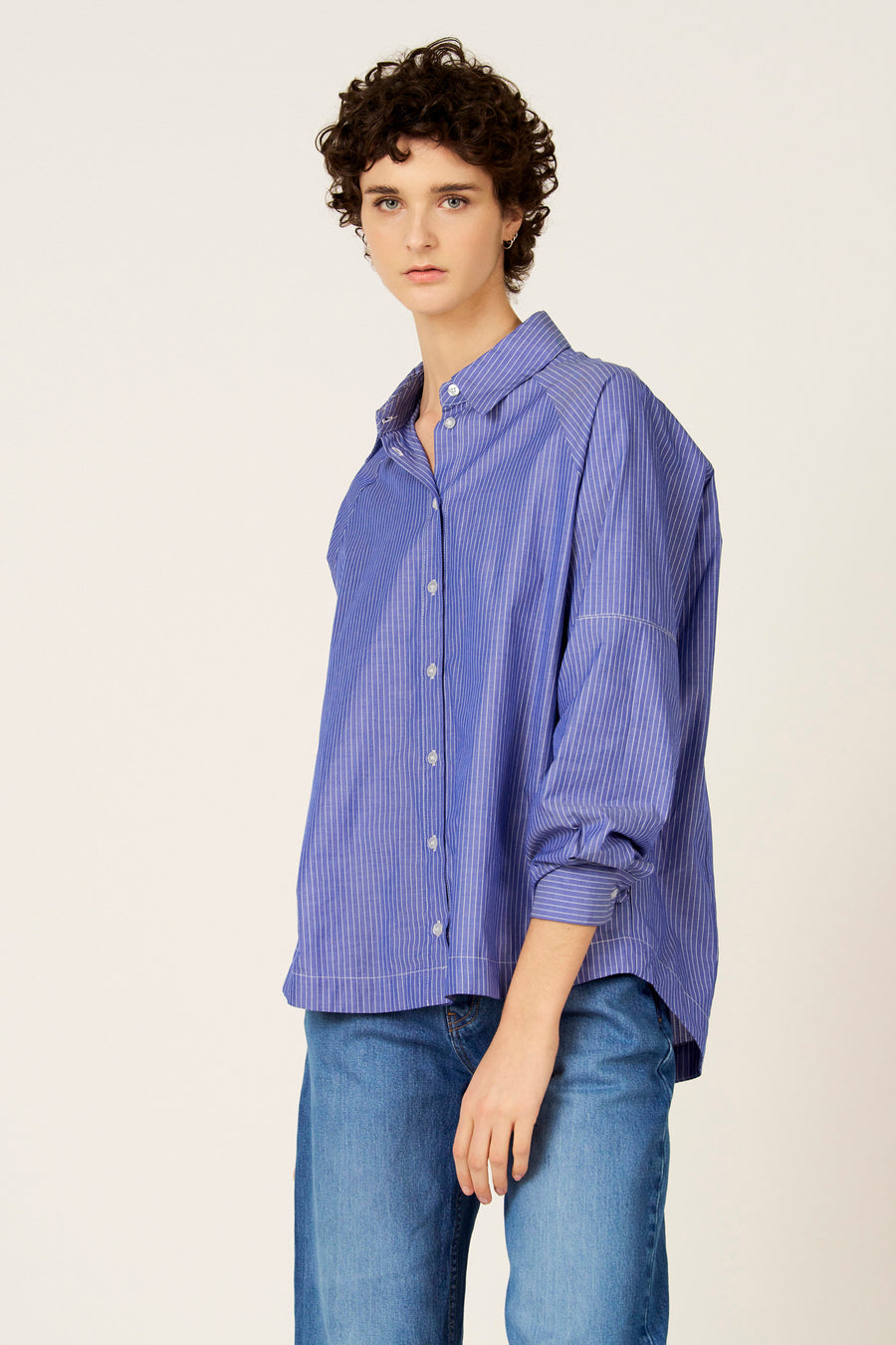Chemise bleue à rayures à manches longues de Le Fabuleux Marcel de Bruxelles, portée avec un jean et des sandales compensées marron.