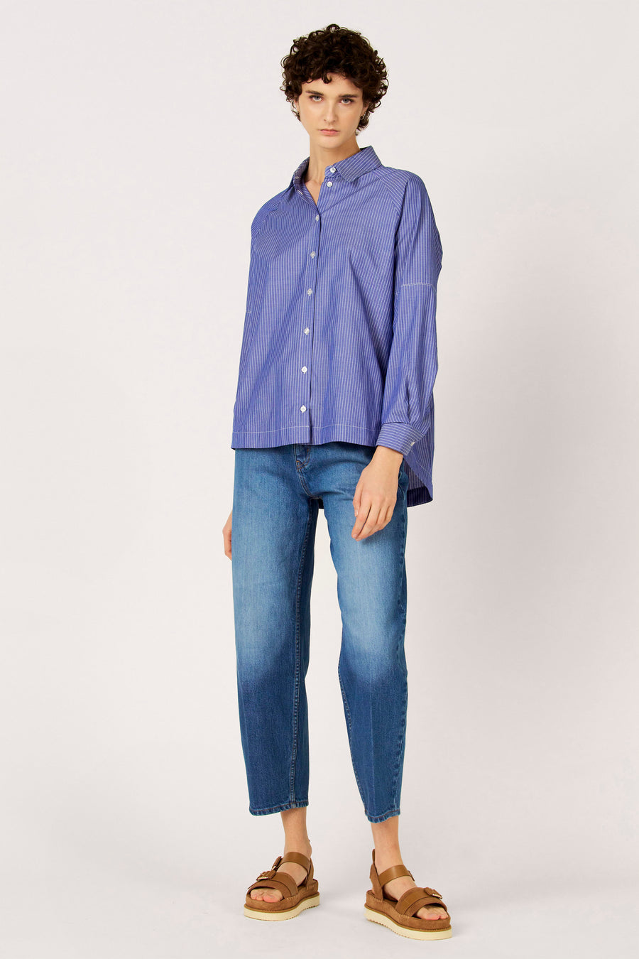 Blauw gestreept hemd met lange mouwen van Le Fabuleux Marcel de Bruxelles, gedragen met jeans en bruine sandalen met plateauzolen.
