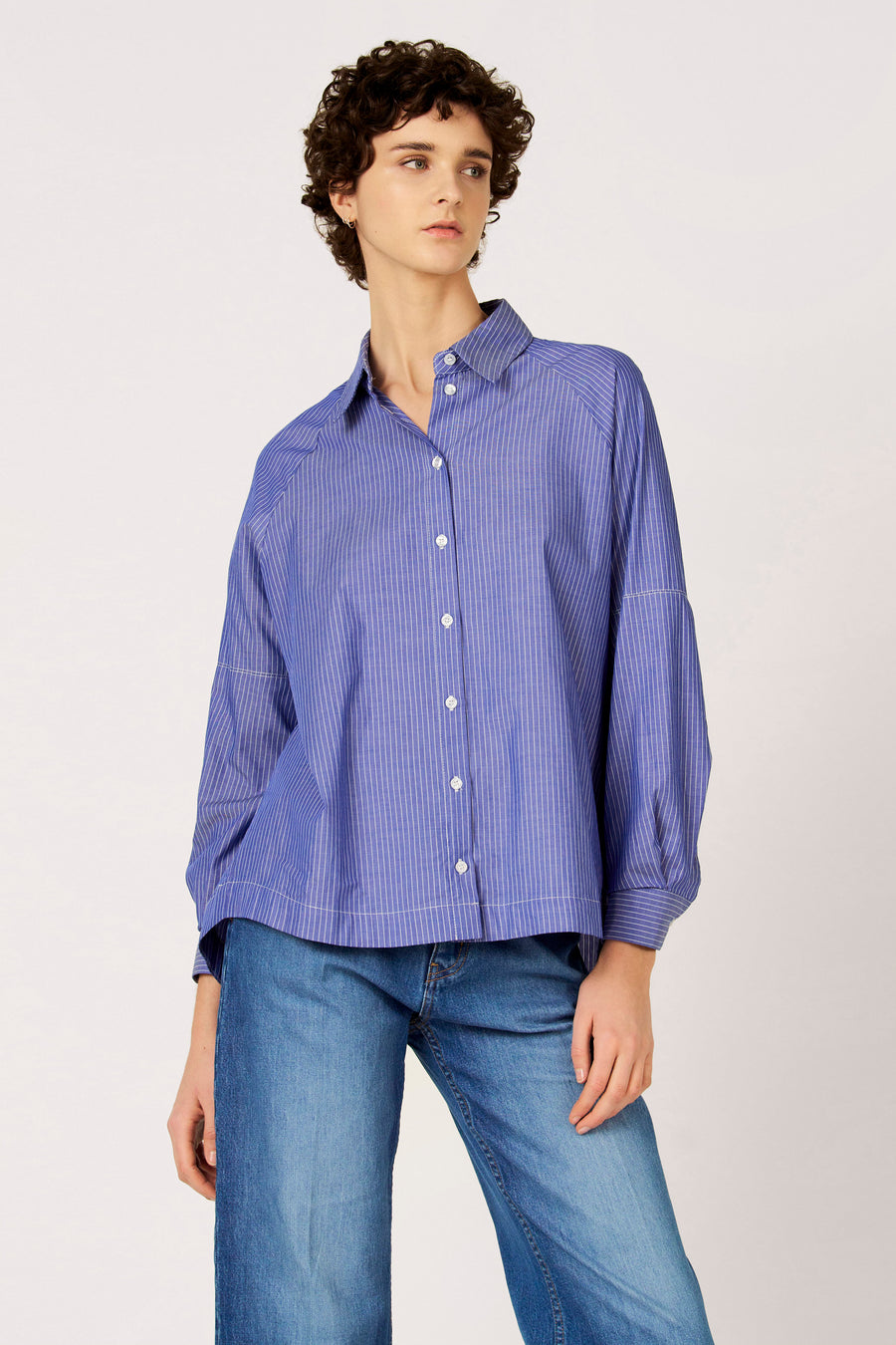 Chemise bleue à manches longues de Le Fabuleux Marcel de Bruxelles, avec un motif à rayures verticales, portée avec un jean.
