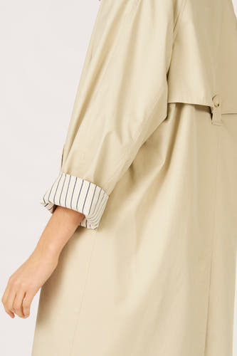 Long manteau beige de Le Fabuleux Marcel de Bruxelles, avec doublure rayée au niveau des manches.