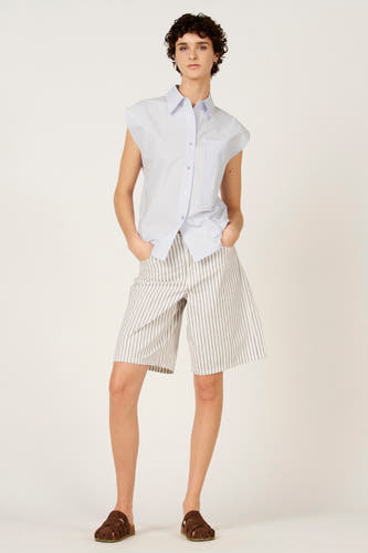 Chemise sans manches bleue de Le Fabuleux Marcel de Bruxelles, portée avec un short rayé et des sandales marron.
