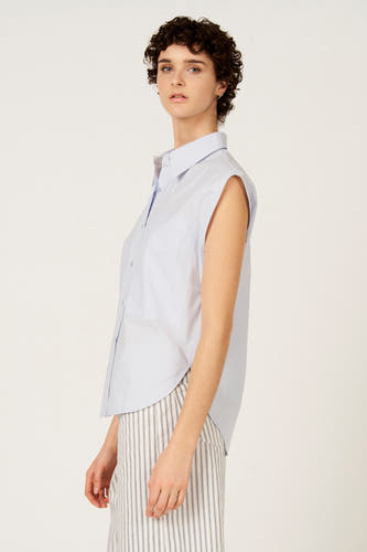 Chemise bleue sans manches de Le Fabuleux Marcel de Bruxelles, avec une poche poitrine et un pantalon à rayures verticales.