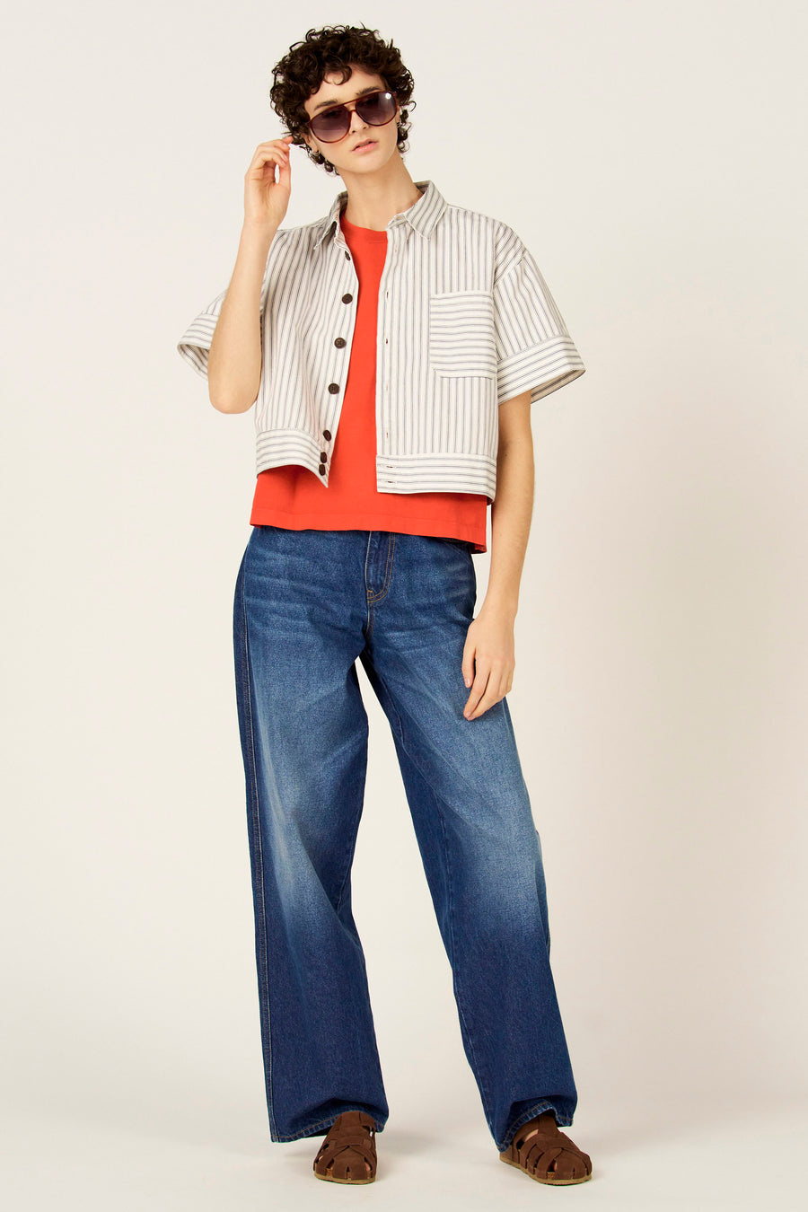 Chemise bleue à rayures à manches courtes de Le Fabuleux Marcel de Bruxelles, portée avec un t-shirt orange et un jean ample.