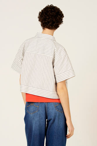 Chemise bleue à manches courtes de Le Fabuleux Marcel de Bruxelles, rayée, portée avec un t-shirt orange et un jean ample.