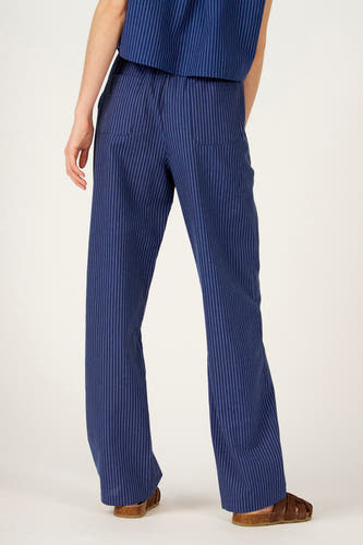 Pantalon bleu de Le Fabuleux Marcel de Bruxelles, avec motif à rayures craie et poches arrière, porté avec des sandales marron.