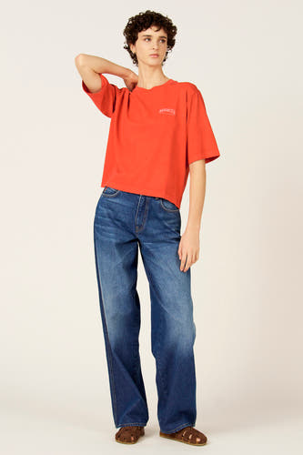 T-shirt rouge à manches courtes de Le Fabuleux Marcel de Bruxelles, porté avec un jean ample et des sandales.