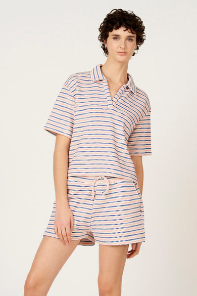 Polo bleu de Le Fabuleux Marcel de Bruxelles, avec des rayures roses et un motif en losange, vu de dos.
