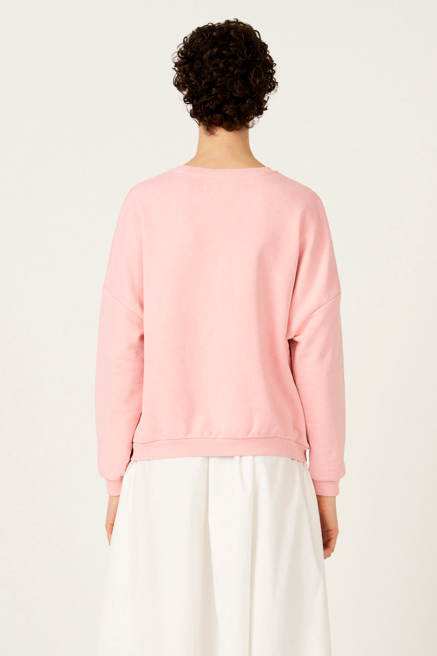 Roze sweater met ronde hals van Le Fabuleux Marcel de Bruxelles, rugaanzicht met witte rok.

