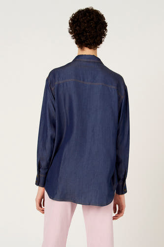 Chemise en jean bleu foncé à manches longues de Le Fabuleux Marcel de Bruxelles, vue de dos, avec surpiqûres marron et pantalon rose.