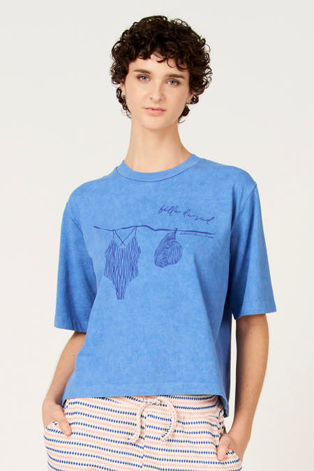 T-shirt bleu à manches courtes de Le Fabuleux Marcel de Bruxelles, avec imprimé graphique d'un maillot de bain sur une corde à linge.