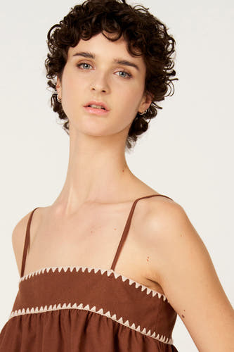 Mouwloze bruine blouse van Le Fabuleux Marcel de Bruxelles, met witte zigzagdetails rond de halslijn.
