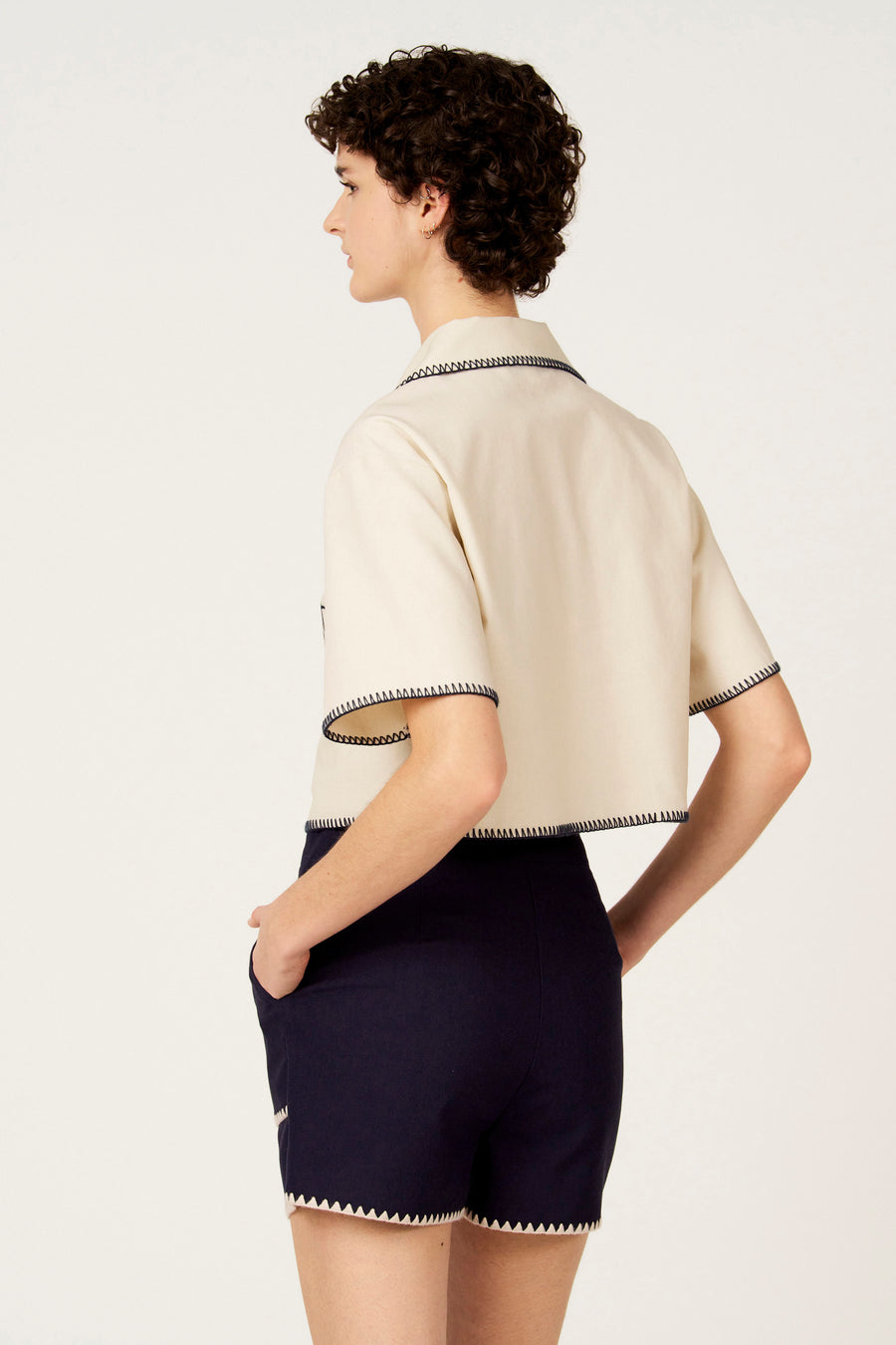 Ecru hemd met korte mouwen van Le Fabuleux Marcel de Bruxelles, afgewerkt met contrasterende stiksels, gedragen met donkerblauwe shorts.

