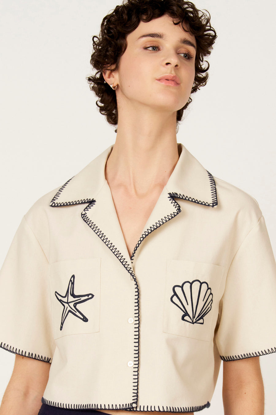Chemise écru à manches courtes de Le Fabuleux Marcel de Bruxelles, avec surpiqûres bleu foncé et motifs marins.