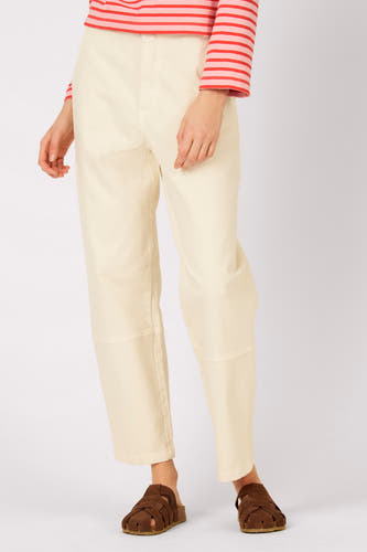 Pantalon écru de Le Fabuleux Marcel de Bruxelles, avec empiècements aux genoux et sandales marron.