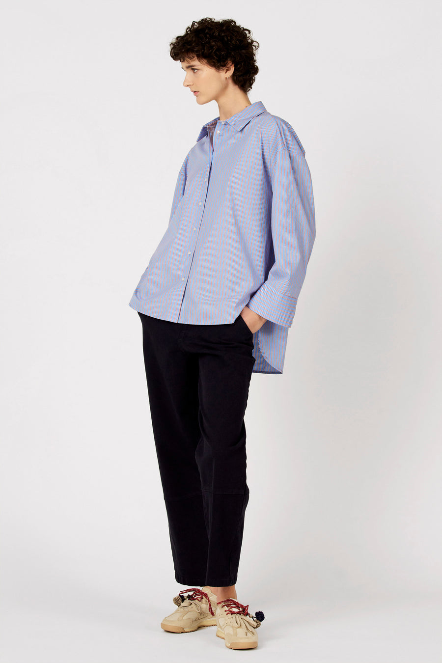 Pantalon bleu de Le Fabuleux Marcel de Bruxelles, porté avec une chemise rayée et des baskets couleur crème.