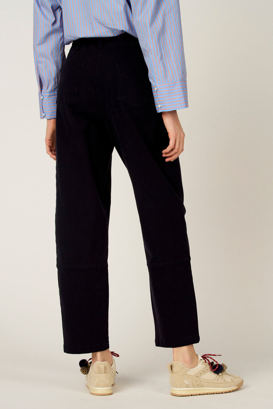 Pantalon bleu de Le Fabuleux Marcel de Bruxelles, vu de dos, combiné avec une chemise rayée et des baskets crème.
