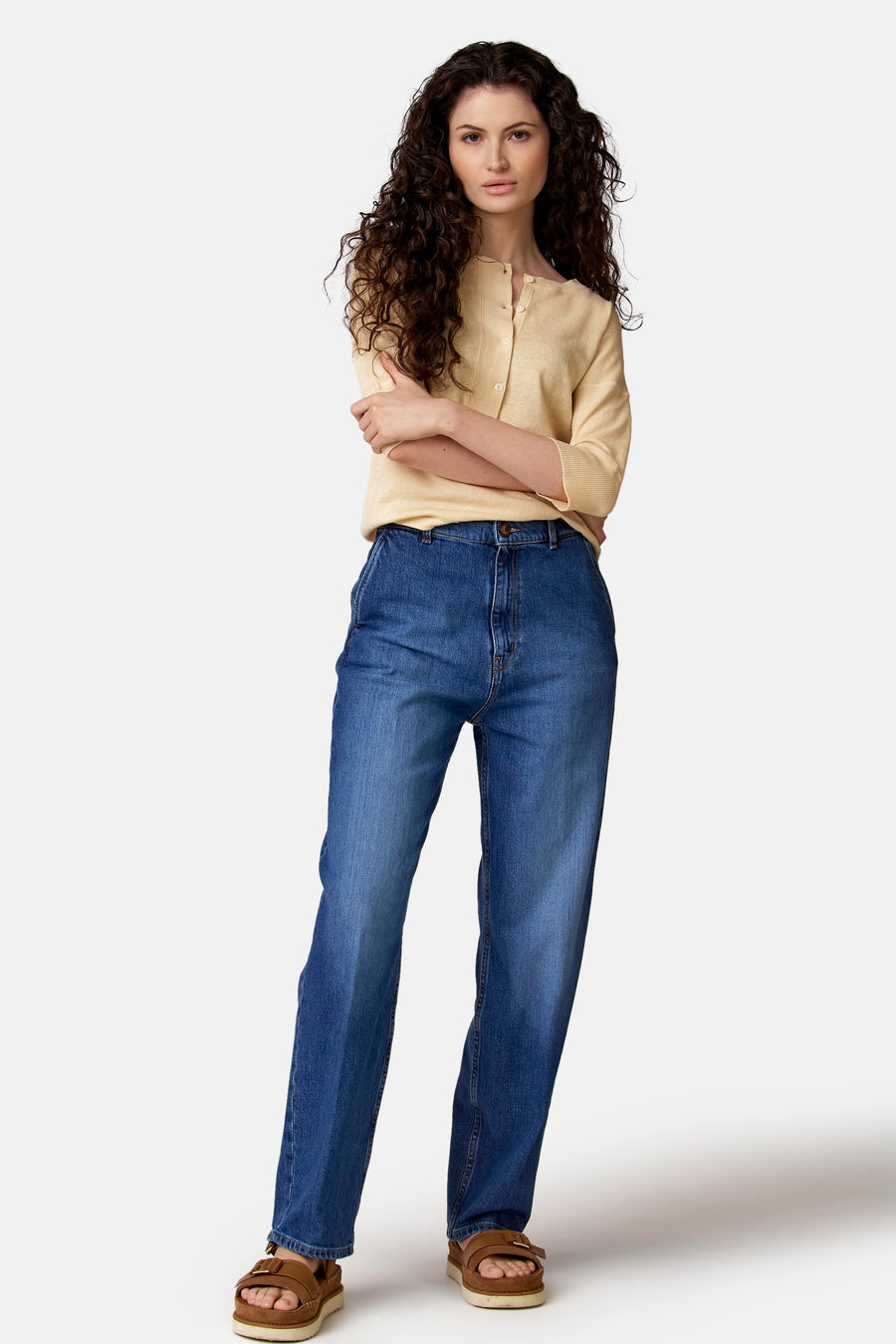 Jean slim-fit en denim foncé de Le Fabuleux Marcel de Bruxelles, combiné avec un gilet jaune et des sandales marron.