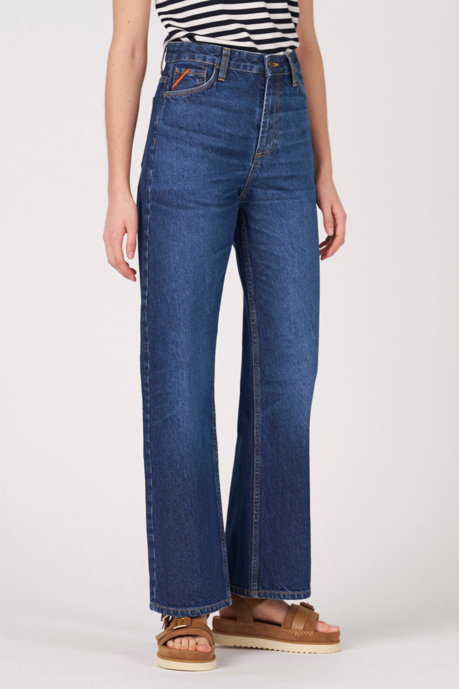 Jean en denim foncé coupe large de Le Fabuleux Marcel de Bruxelles, avec taille haute et sandales marron.