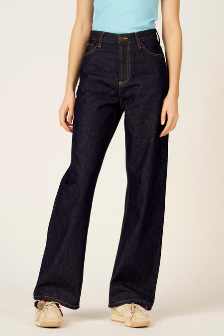 Wijde denim jeans van Le Fabuleux Marcel de Bruxelles, met oranje stiksels en beige sneakers.
