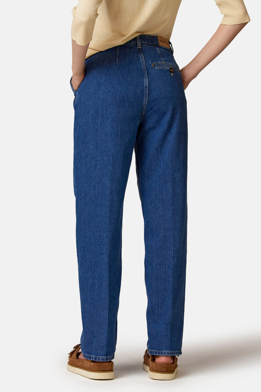 Jean en denim foncé de Le Fabuleux Marcel de Bruxelles, avec une poche arrière et des chaussures décontractées.