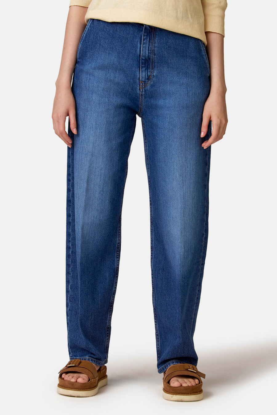 Jean slim fit en denim foncé de Le Fabuleux Marcel de Bruxelles, avec une jambe droite et des sandales marron.