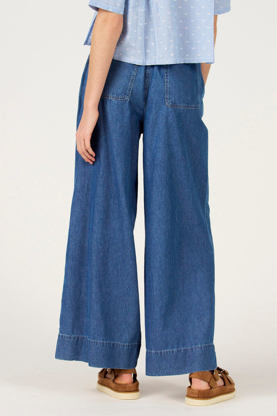Wijde jeans van blauw denim van Le Fabuleux Marcel de Bruxelles, met zakken en bruine sandalen.
