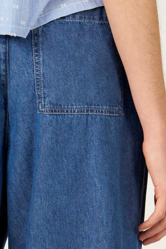 Jeans coupe large en denim bleu de Le Fabuleux Marcel de Bruxelles, avec poche plaquée, combinée avec une chemise rayée.