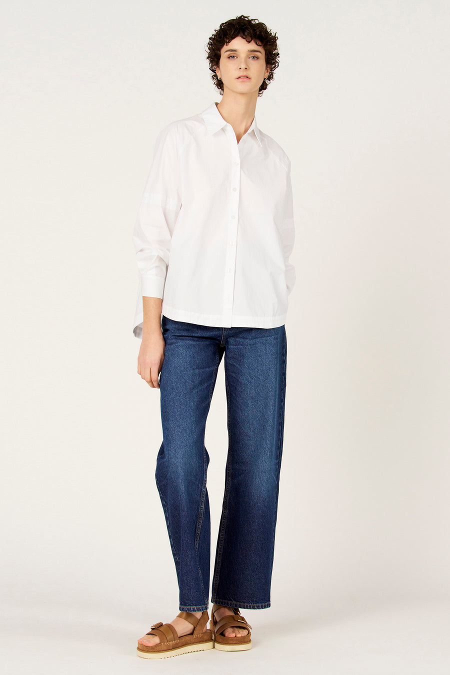 Chemise blanche à manches longues de Le Fabuleux Marcel de Bruxelles, portée avec un jean bleu foncé et des sandales compensées marron.
