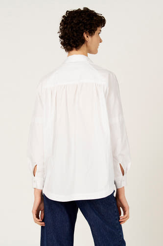 Chemise blanche à manches longues de Le Fabuleux Marcel de Bruxelles, vue de dos, avec un jean bleu.