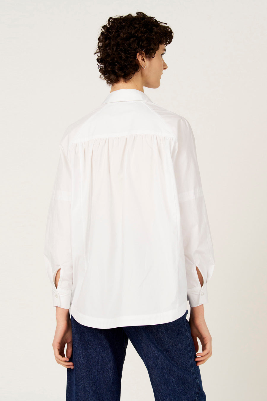 Chemise blanche à manches longues de Le Fabuleux Marcel de Bruxelles, vue de dos, avec un jean bleu.